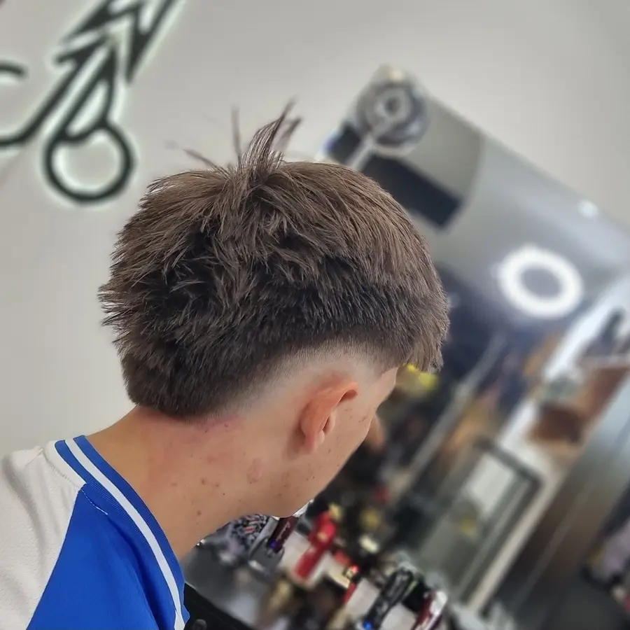 Corte con diseño en línea realizado en El Jordy Barbershop, con el símbolo de tijeras del local visible al fondo